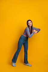 Bright confident young woman in a trendy blue patterned top and jeans poses playfully against a...