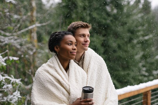 Diverse couple enjoying winter hike while wrapped in blankets in the snow