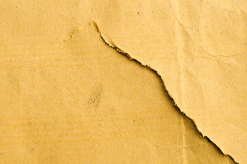 Full frame macro of old, crumpled brown kraft paper with a rough diagonal torn edge. Represents vintage texture, grunge background, packaging, decay, and recycled paper concept.
