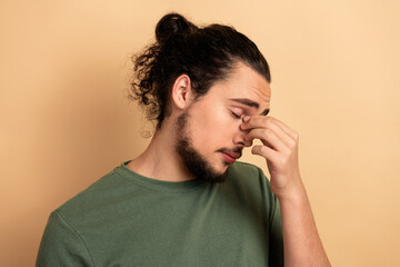 Young male mixed race model with long hair and beard wearing a green t shirt expressing stress and fatigue against a beige background