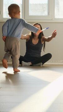a child with bare legs runs across the floor to his mother against a sunny window, hugging mom happy family first steps towards his family at the window of the house