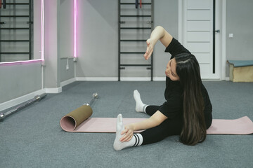 Young Asian woman is stretching yoga workout on exercise mat in sport room.
