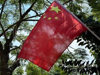 Chinese flag waving in the wind against a backdrop of lush green foliage.