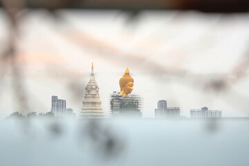 Big golden Seated Buddha on a blurred foreground. Statue Buddha in bangkok. A large Buddha statue in the middle of the city. There is scaffolding surrounding as construction is not yet complete.
