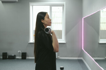 Strong beautiful fitness asian woman training, doing exercise with dumbbells at gym. Female sport athlete coach making workout bodybuilding on bench heavy fit equipment.