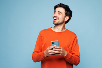 Young fun Caucasian man he wear orange sweatshirt casual clothes hold in hand use mobile cell phone...