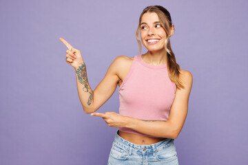 Young happy smiling woman she wear pink tank top casual clothes point index finger aside on blank...