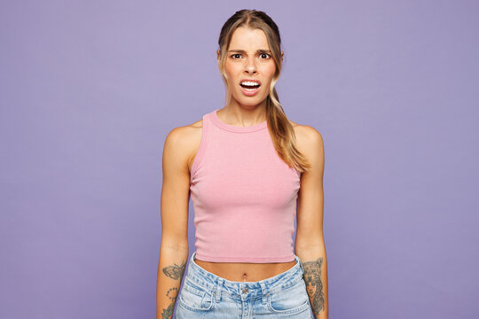 Fototapeta Young sad dissatisfied angry disappointed mad woman she wearing pink tank top casual clothes looking camera isolated on plain pastel light purple wall background studio portrait. Lifestyle concept.