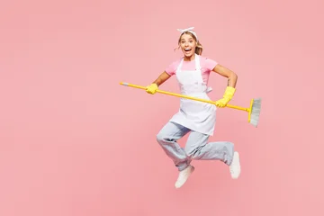 Fotobehang Muziek Full body young shocked surprised happy woman she wearing white apron hold broom sweeping while doing housework tidy up jump high isolated on plain pastel light pink background. Housekeeping concept.  © ViDi Studio