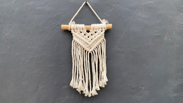 Macrame wall hanging made of simple knitted white wool on a wooden and black wall background