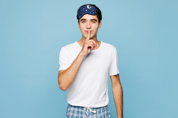 Calm young man he wear pyjamas jam sleep eye mask rest relax at home say hush be quiet with finger on lips shhh gesture isolated on plain pastel light blue cyan background Good mood night nap concept