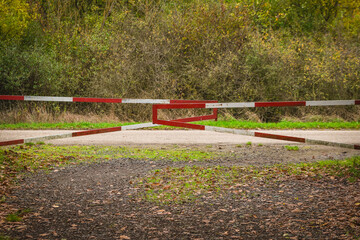 Path blocked with a red and white barrier surrounded by lush greenery in a peaceful forest area on a crisp autumn day