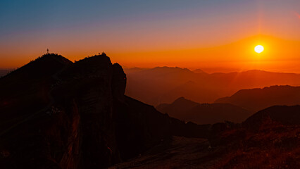 Alpine sunset or sundowner with hiker silhouettes and a summit cross at Mount Diedamskopf, Schoppernau, Bregenz, Vorarlberg, Austria