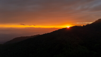 Sunrise over mountain peak with warm orange sky and peaceful clouds, morning light in Thailand highland, beautiful tropical landscape nature background.