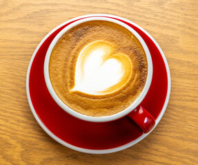 Top view of cappuccino with heart latte art in red cup on wooden table. Ideal for coffee shop promotions, breakfast menus, blogs, cafe lifestyle content, or cozy drink visuals.