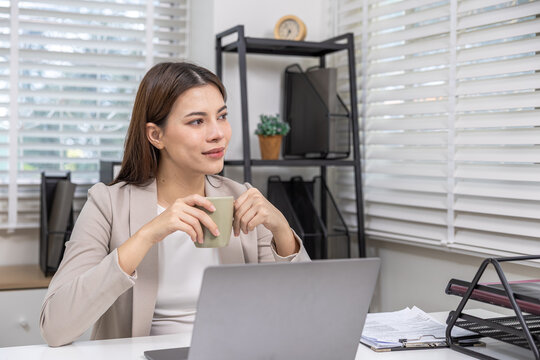 Asian businesswoman in office sitting at desk with laptop, thoughtful, confident about work project or business plan, representing smart business owner, leadership mindset and professional motivation