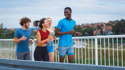 Fototapeta premium Smiling group of people running together on outdoor road.