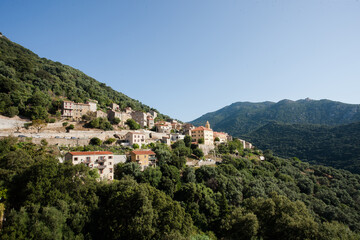 Fototapeta premium Landscape view of Cargèse village in Corsica, France. Traditional Mediterranean houses in green mountain scenery under a bright summer sky. Beautiful travel destination in southern Europe.