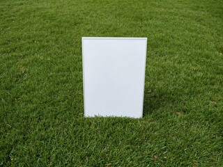 Blank vertical white sign mockup standing on a lush green grass lawn. Simple outdoor display board template.