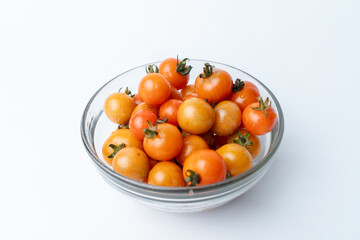 A clear glass bowl filled with fresh, ripe cherry tomatoes. Isolated on a clean white studio background. Healthy food ingredient. Ample copy space.
