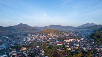 Obraz premium High aerial drone footage of the town of Bajawa, Flores, Indonesia. The town is in a valley surrounded by mountains at golden hour sunrise. 