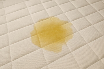 Frustrating yellow pee stain from urine on wet white mattress. bedwetting accident creating dirty mess, domestic cleaning problem on surface of bed