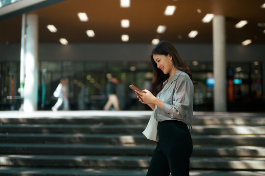 Young woman smiling, walking, using mobile phone