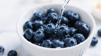 Fresh blueberries being washed in a white bowl, water droplets clinging to the fruit