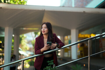Asian woman thinking while holding phone outdoor