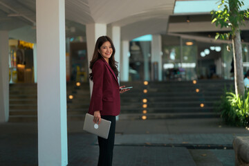 Asian businesswoman smiling holding laptop and phone outdoors