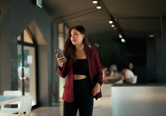 Asian businesswoman holding phone looking forward in modern office