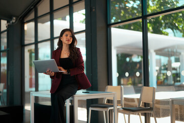Asian businesswoman holding laptop contemplating looking through window