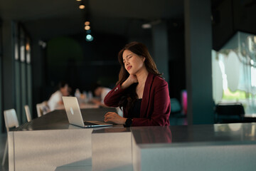 Woman feeling neck pain working on laptop in office
