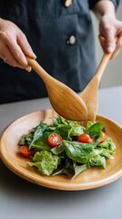 Close Up Shot of a Person Tossing Mixed Greens with Wooden Tongs. Arranging a Healthy Salad Plate in a Contemporary Kitchen. Clean Food and Mindful Eating Concept. 