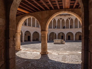 Castell de Bellver. Palma de Mallorca, historic courtyard features a circular design with stone arches and a central fountain, bathed in sunlight, Majorca