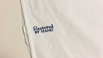 Restored by hand embroidered message stitched in blue thread on white cloth edge