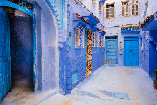 A vibrant blue courtyard with ornate windows and doors under a bright sky. Chefchaouen, Morocco