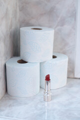 Red lipstick and toilet paper rolls on white bathroom surface