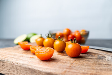 Close-up of fresh cherry tomatoes, whole and sliced, on a rustic wooden cutting board. A knife, bowl, and limes are in the soft bokeh background. Concept for fresh ingredients, cooking, and healthy re