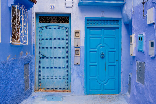 Vibrant blue doors and walls in a narrow alleyway with ornate metalwork. Chefchaouen, Morocco