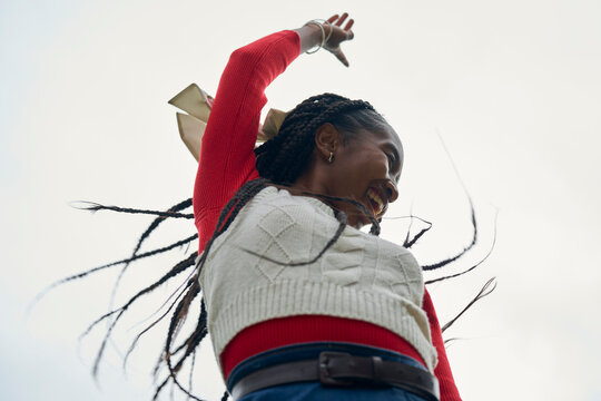 Smiling woman with braided hair and a red sweater against a light sky background. Bruges, Belgium - Powered by Adobe
