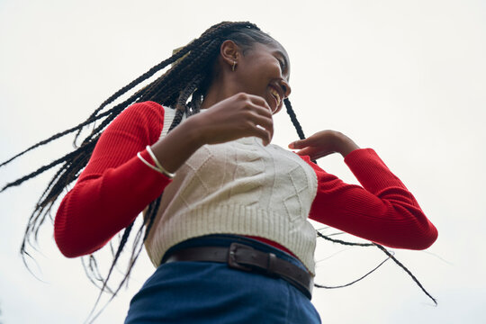 Woman in sweater and long braids smiles under a clear sky, viewed from a low angle. Bruges, Belgium