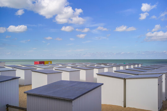 Rows of white beach huts with grey roofs under a blue sky with clouds by the sea. Blankenberge, West Flanders, Belgium