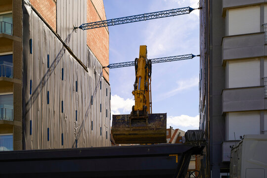 Excavator between two buildings at a construction site under a clear blue sky. Blankenberge, West Flanders, Belgium