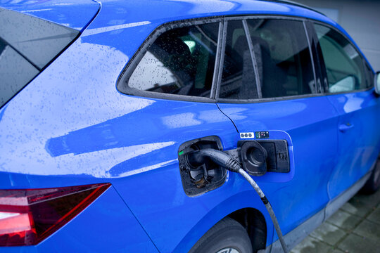 Blue electric car charging at a wet charging station on a rainy day. Blankenberge, West Flanders, Belgium