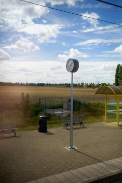 Empty train station platform with a large clock under a bright blue sky, seen from inside the passing train. Blankenberge, West Flanders, Belgium