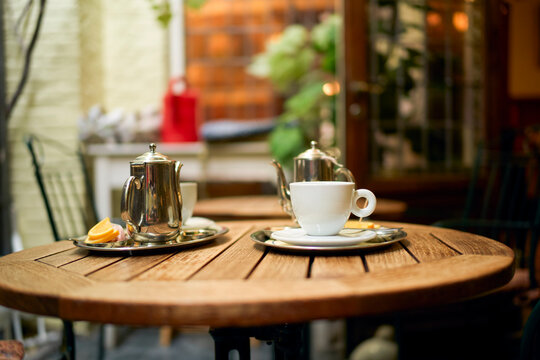 Outdoor cafe table with teapots, cup, and lemon slice on a wooden surface. Bruges, Belgium