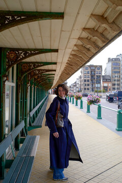 Woman in a blue coat walking along a covered walkway lined with benches and flowers. Blankenberge, West Flanders, Belgium