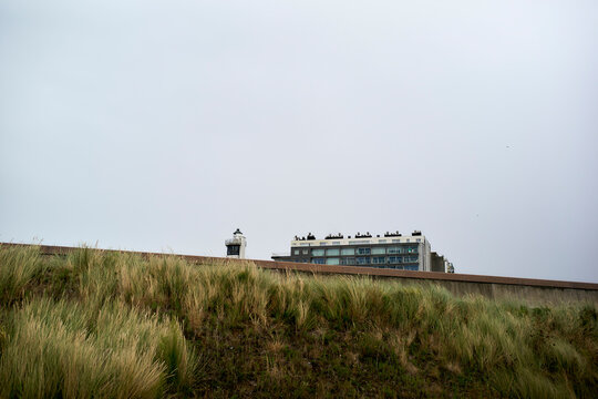 Lighthouse and modern building behind grassy dunes under a cloudy sky. Blankenberge, West Flanders, Belgium