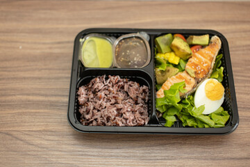 Lunch box with salmon and vegetables in a plastic tray placed on a wooden table.